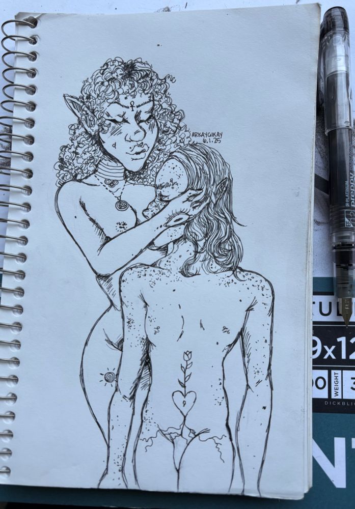A picture of my sketchbook page, on which I’ve drawn two nude elves in ink with my preppy fountain pen. They’re standing next to each other while one holds the others head in one hand and makes a kissy face towards the others forehead. The one doing the kissing face has curly hair and the other one, who is covered in freckles, has straight hair. They both have nipples rings and tattoos. The freckled one has a large tattoo on her belly of a heart around her bellybutton and a tulip sprouting from the heart, with the roots reach below their waist line to their thighs. The curly haired one has an ankh tattooed on her forehead, and a sun tattooed on her thigh. She is wearing two necklaces, one that’s a medallion on a chain and the other that’s a layered choker made of metal hoops and three encased pendants soldered to the lowest of the hoops. 