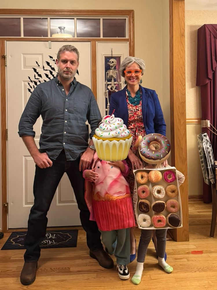 A man in a Paul Hollywood costume, a woman in a Prue costume, and two kids dressed as a cupcake and box of donuts respectively 
