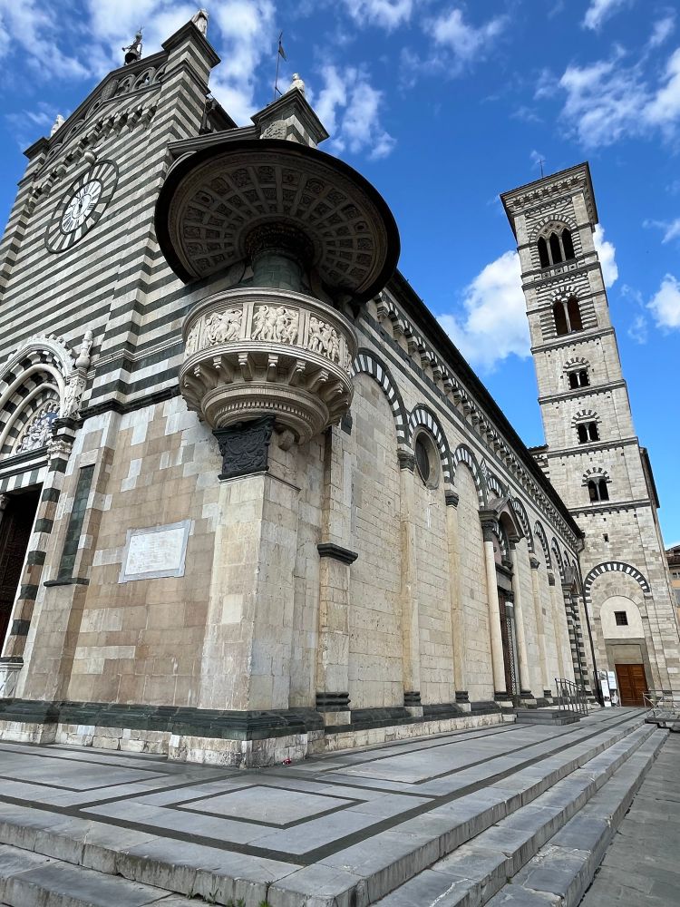 Renaissance sculpture several metres off the ground - like a little balcony with a roof - on the corner of a Romanesque/Renaissance church (striped stone facade) with a bell tower behind 
