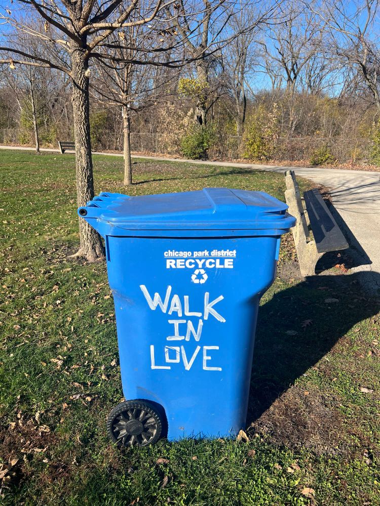 A blue Chicago Park District Recycle bin with the words “WALK IN LOVE” painted on its side, in Gompers Park, Chicago.