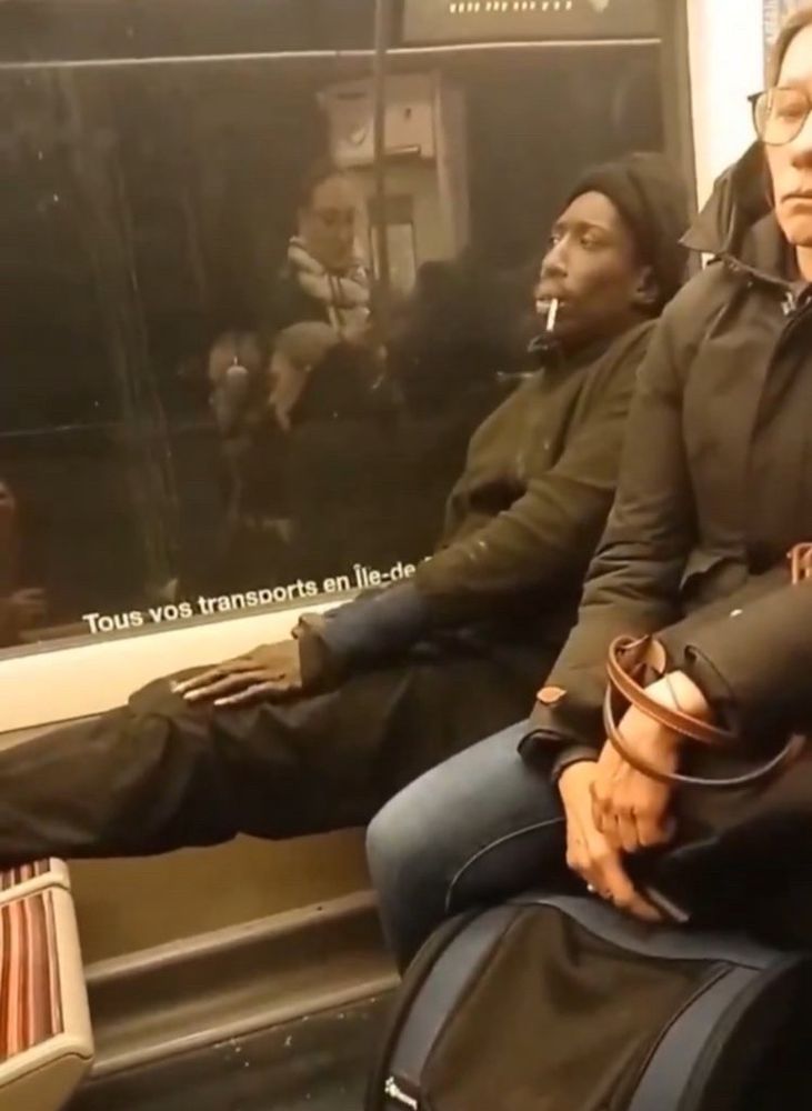 screenshot of the video. a black dude absolutely frenching out on public transit. he has his feet up and is pounding a cigarette, looking disinterested. he’s wearing a beret. this is the most french shit you’ve ever seen. he might as well be dressed as a mime 