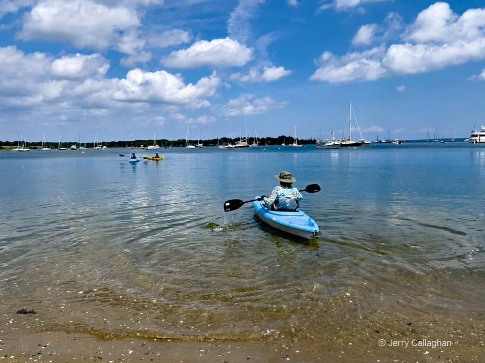 Kayaking in Wickford, RI
A kayaker sets off to catch up with two friends also in kayaks.  Many small sailboats are moored in the bay.  White puffy clouds fill the blue sky.

