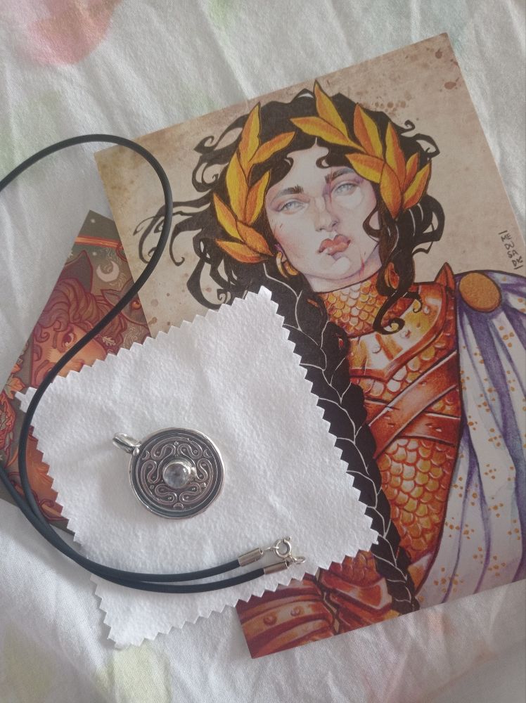 Imagen de un medallón con una piedra lunar en el centro que representa el strophalos de Hékate. Está encima de una ilustración. 