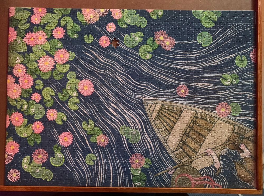 Puzzle missing one piece showing pink flowers, green lily pads, water waves, and a person paddling a canoe 