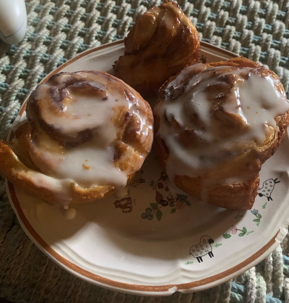 Two and half large cinnamon rolls on a white plate covered in white icing on top of a light blue and white woven table.