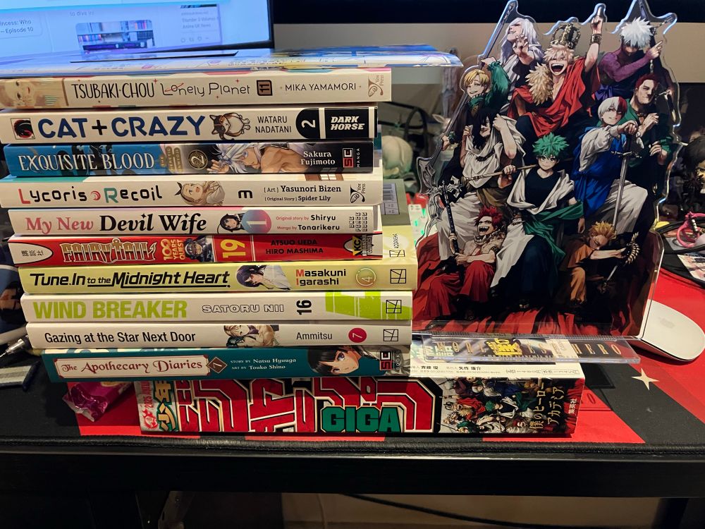 A copy of Shounen Jump Giga with a pile of 10 books on top as well as a My Hero Academia standee 