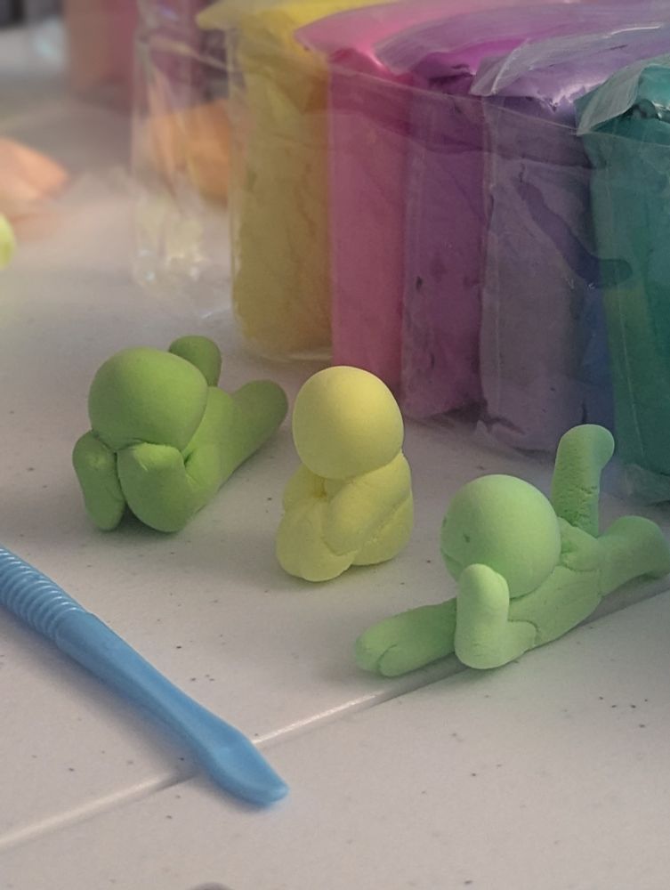 Three handmade smiskis (crafted with air dry clay) they're laying and sitting. Hanging out as friends. Each one crafted by three different people 