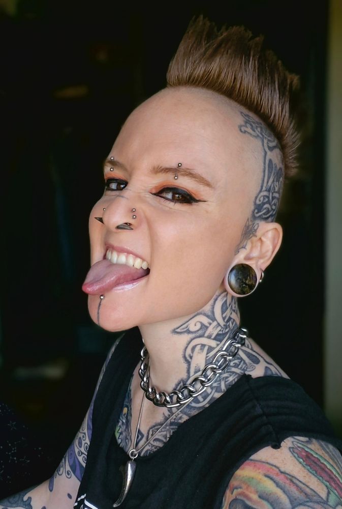 a photo of pye irl, they have lots of piercings, tattoos and a red mohawk