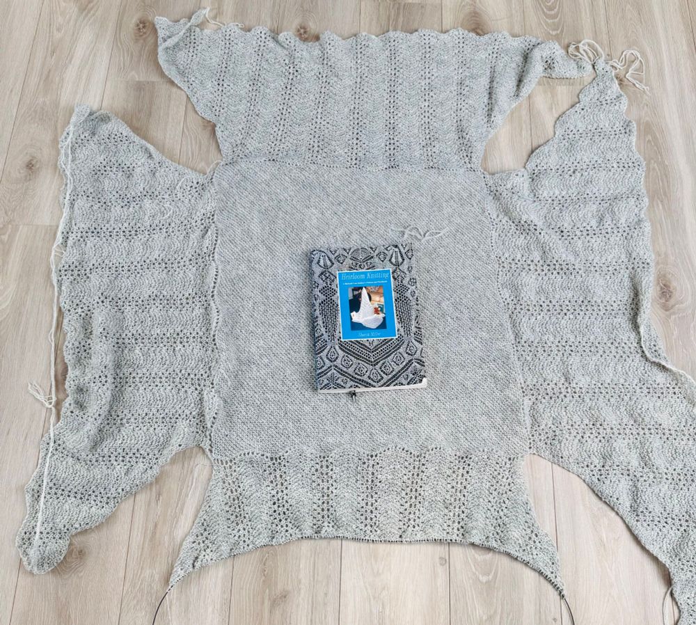 A knitted hap shawl. Centre and three borders complete, fourth border in progress. No edging yet. Sharon Miller’s book ‘Heirloom Knitting’ in the middle to show size. 