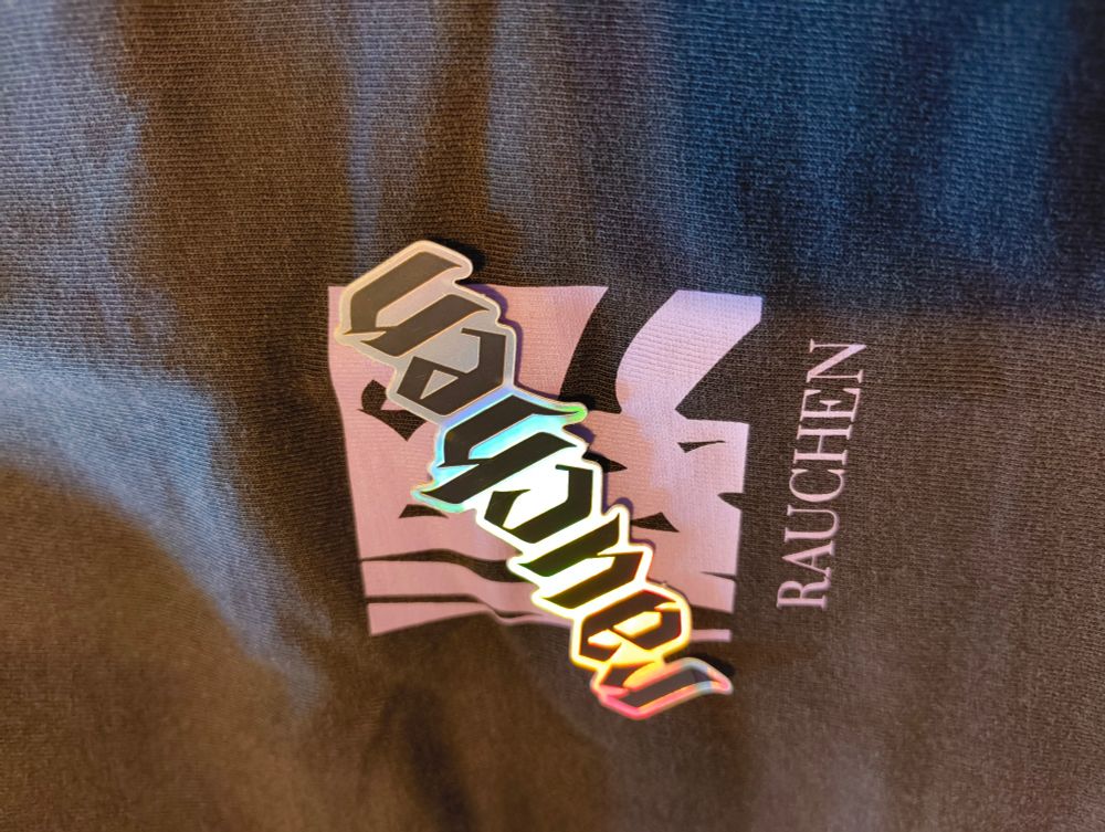 Bild des Brustdruck meines neues rauchen Shirts. darauf liegt ein Regenbogen Glanz Sticker mit dem Text rauchen in gebrochener Schrift 