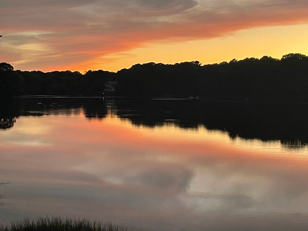 Sunset over trees and water, orange and yellow sky.