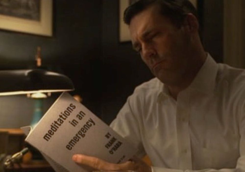 Don Draper reading MEDITATIONS IN AN EMERGENCY by Frank O’Hara by a desk lamp in MAD MEN