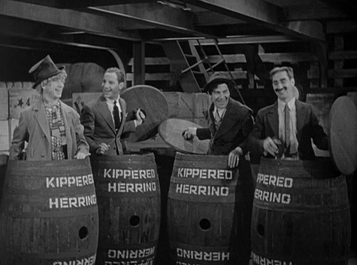 The four Marx Brothers--left to right, Harpo (in top hat), Zeppo, Chico, & Groucho--standing inside open-topped barrels labeled KIPPERED HERRING in a still from MONKEY BUSINESS (1931)