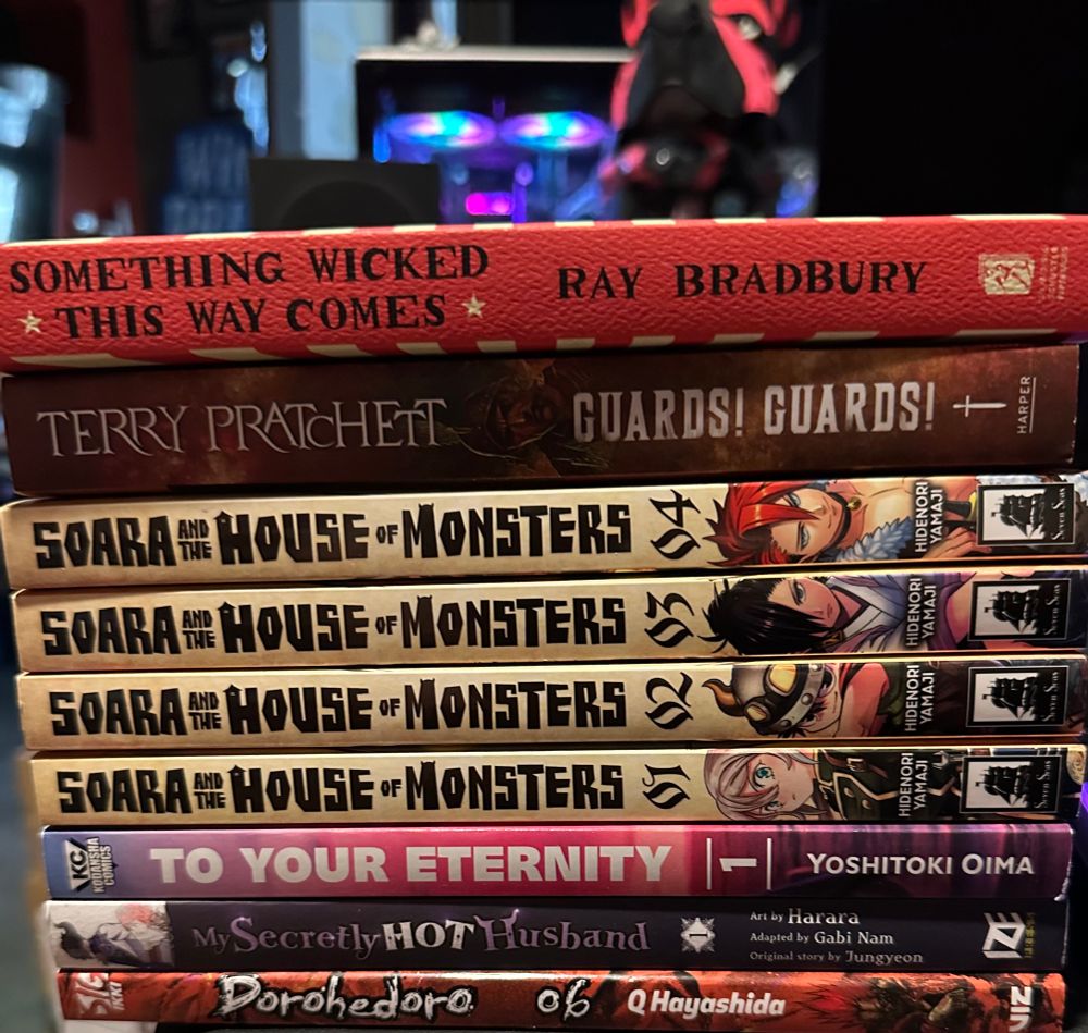 Stack of books including Something Wicked This Way Comes by Ray Bradbury, Guarda! Guards! by Terry Pratchett (I lost my copy years ago and never got to finish it!) volumes 1-4 of Soara House of Monsters, To Your Eternity, My Secretly Hot Husband, and vol 6 of Dorohedoro