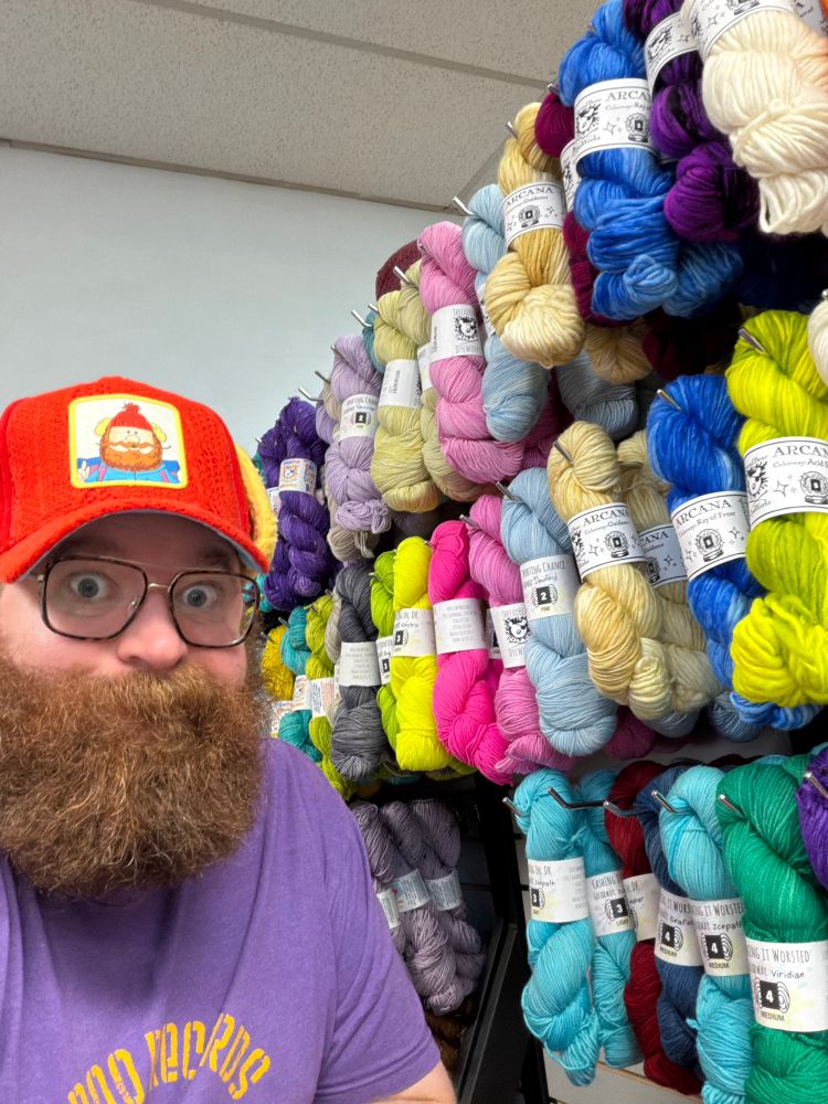 Photo of me next to a wall of yarn that I helped dye or dyed myself. Countless colors!