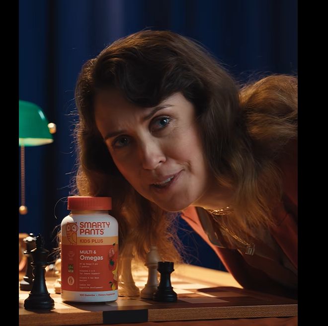 The mom holding a bottle of Smarty Pants vitamins and leaning over the chess board