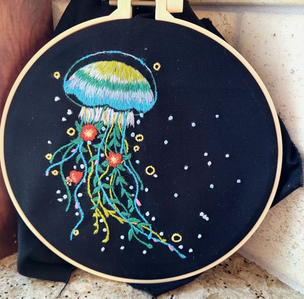 Black background with a jellyfish embroidered in bright greens, blues, and yellow mixed with orange flowers. 