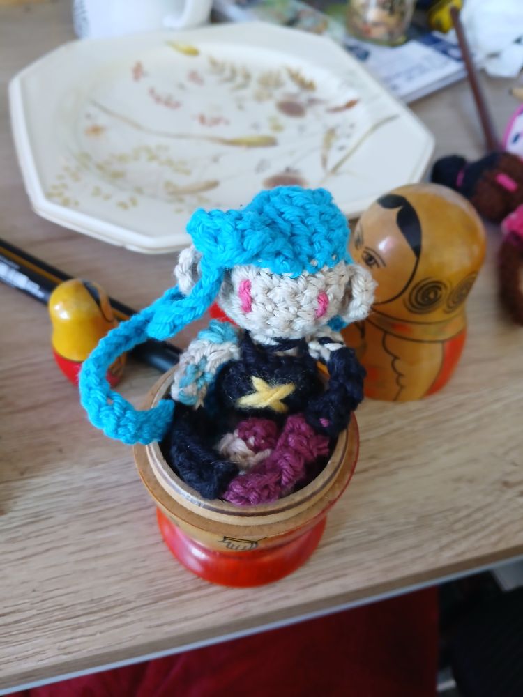 Crochet doll of Jinx huddled in half a matryoshka doll