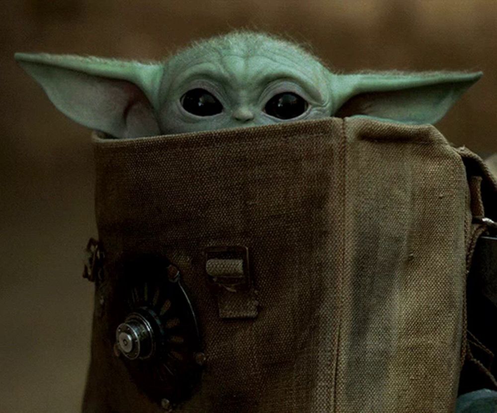 a baby yoda looks out of a brown bag