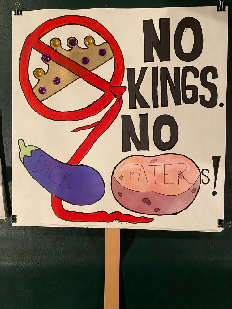 Home made protest sign with an image of a gold bejeweled crown, a red circle drawn around it with strikethrough, that turns into an obnoxiously long red tie trailing the bottom of the sign. The sign reads in bold black capital letters, "NO KINGS. NO [image of eggplant emoji with "DICK" written on it] [image of potato emoji with "TATER"]s!"