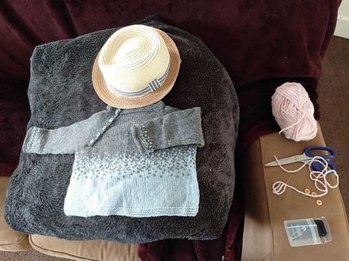 Gray and blue side buttoned infant sweater with a straw trilby hat.