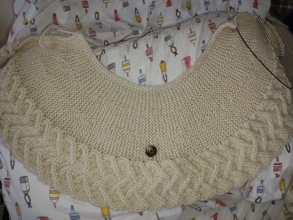 Cardigan yoke spread out. Cardigan is being knit sideways. Metal button placed for perspective.