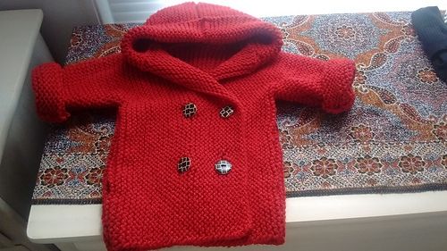 Red wool duffle coat with giraffe print buttons. Coat is knit from sleeve to sleeve with a hood picked up and knit after the body is complete.