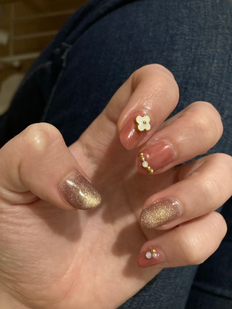 hand with nails painted pink with and topped either with a gold shimmer or gold and white flower decorations or beads