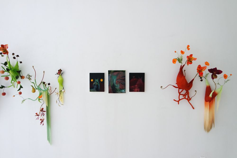 A set of green and reddish wall sculptures, with three dark-toned paintings in the middle