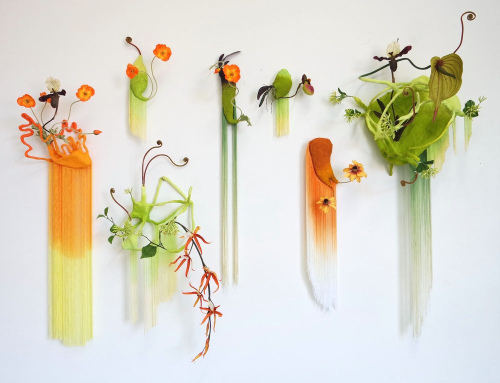 A set of green and orange wall sculptures with flowers and fringe