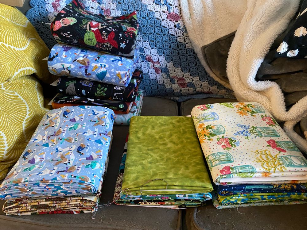 Four small, neat stacks of fabric on a couch. 