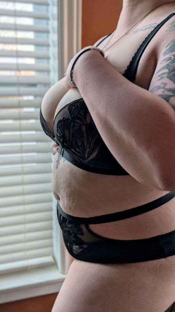 A woman standing in front of a window in two-piece lingerie, with one hand on her chest