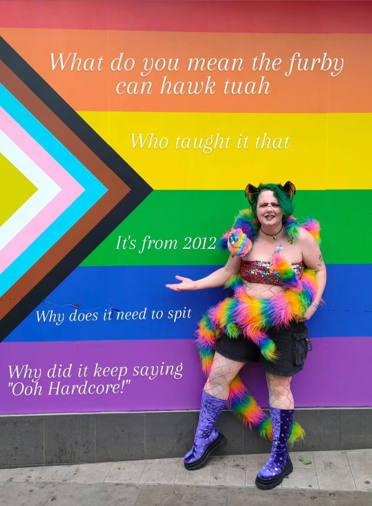 A giant progress pride flag with a green haired person posing in front of it looking disgusted, they're wearing a sequin bandeau bra, black cargo shorts, velvet blue star boots, rainbow dragon ears, and also a 10ft long 8 legged furby wrapped around their body.
There is text on the pride flag stripes that read
"What do you mean the furby 
can hawk tuah

Who taught it that

It's from 2012

Why does it need to spit

Why did it keep saying
"Ooh Hardcore!""