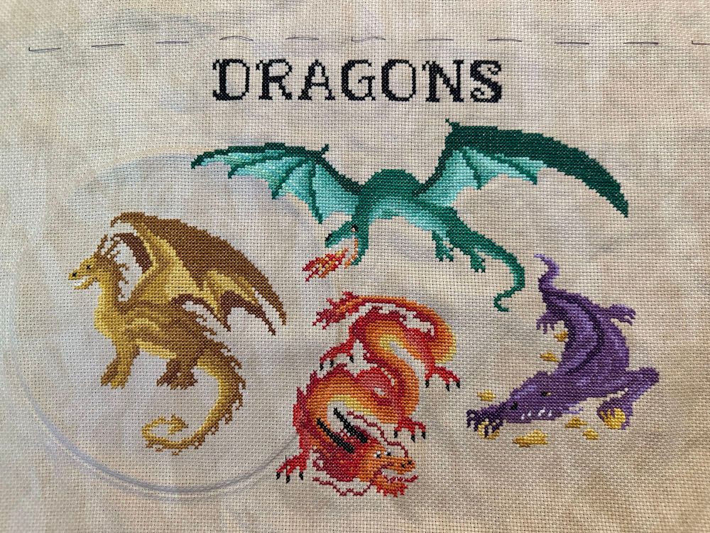 Four dragons (green, purple, red, and gold) cross-stitched under the word dragons