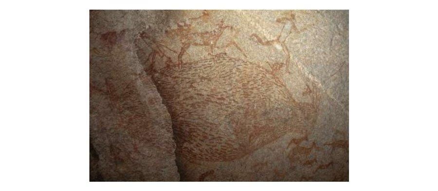 Digital photograph (colour); view of painted rock art on a rock face showing oval-like shape (net?) outlined in red and infilled by red fishes. The shape is surrounded by several human figures and animals, most of them antelopes infilled in red and depicted upright facing right. The human figures are outlined or infilled in red, mostly depicted upright facing right and in some cases with the legs splayed as if running. Matobo Hills, Zimbabwe.
