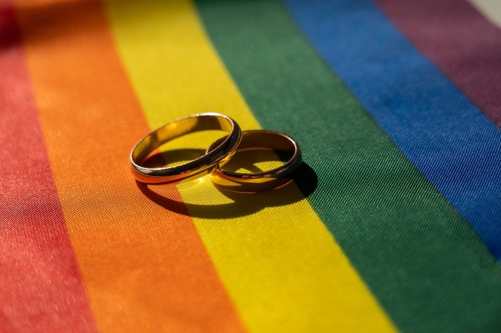Two gold wedding rings rest on a rainbow-striped fabric, symbolizing LGBTQ+ pride and marriage equality.