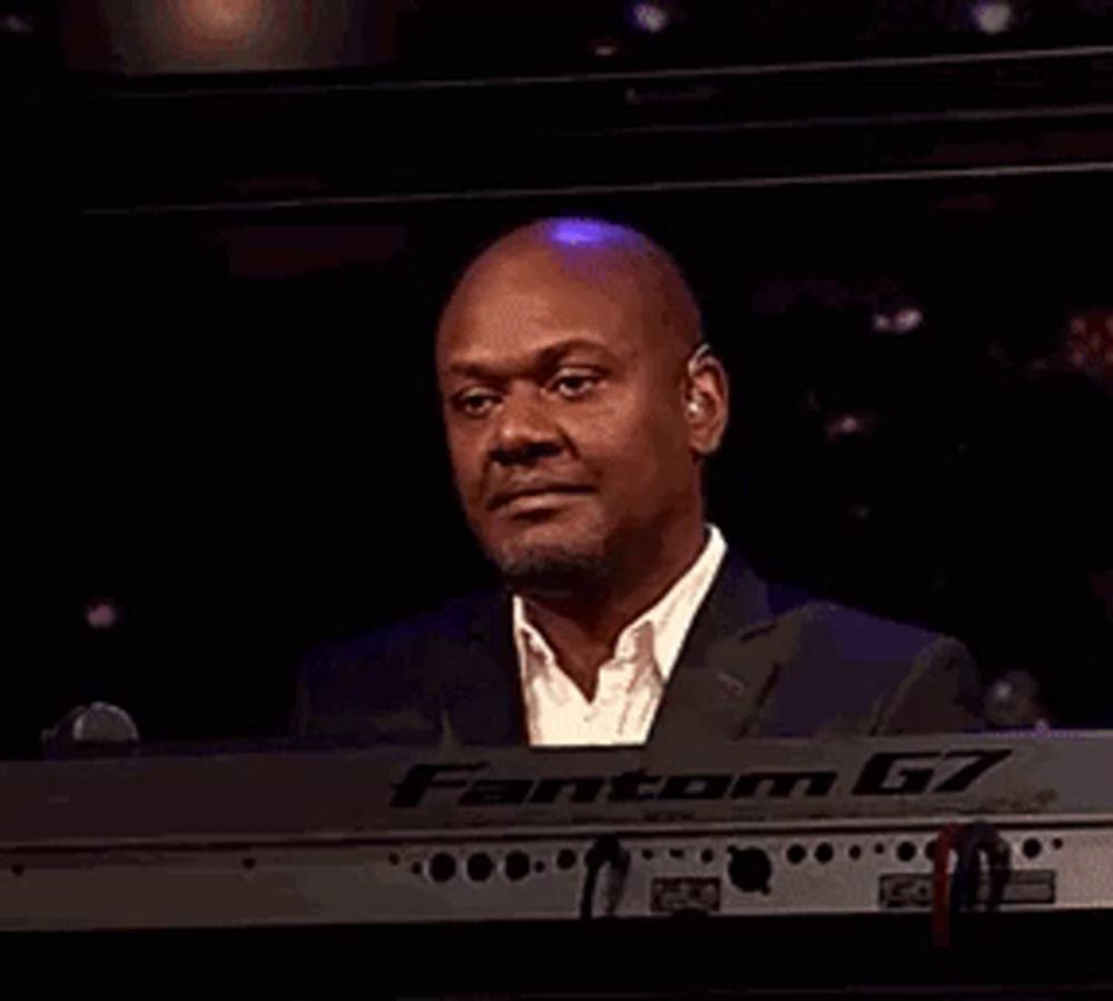 a man in a suit is laughing while playing a keyboard in a dark room .