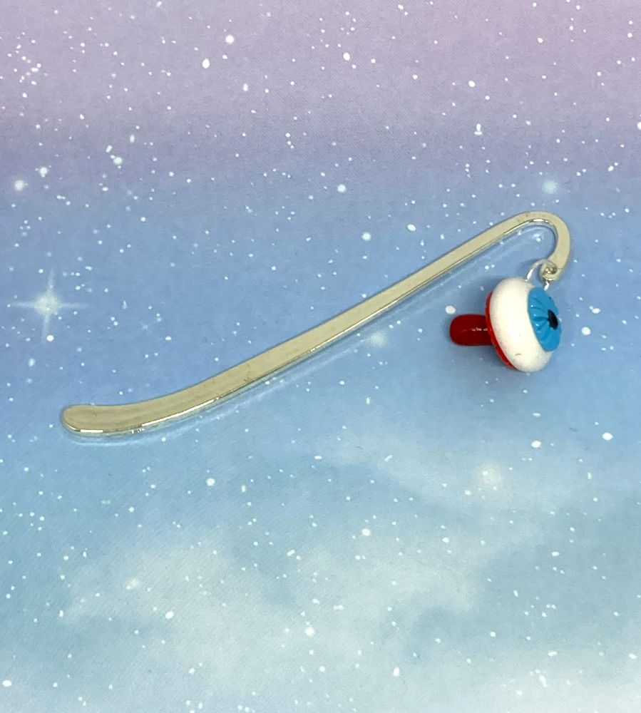 Photo of a polymer clay charm on a silver bookmark hook laid out. The charm is facing the right and is that of a mushroom made to look like an eyeball.
