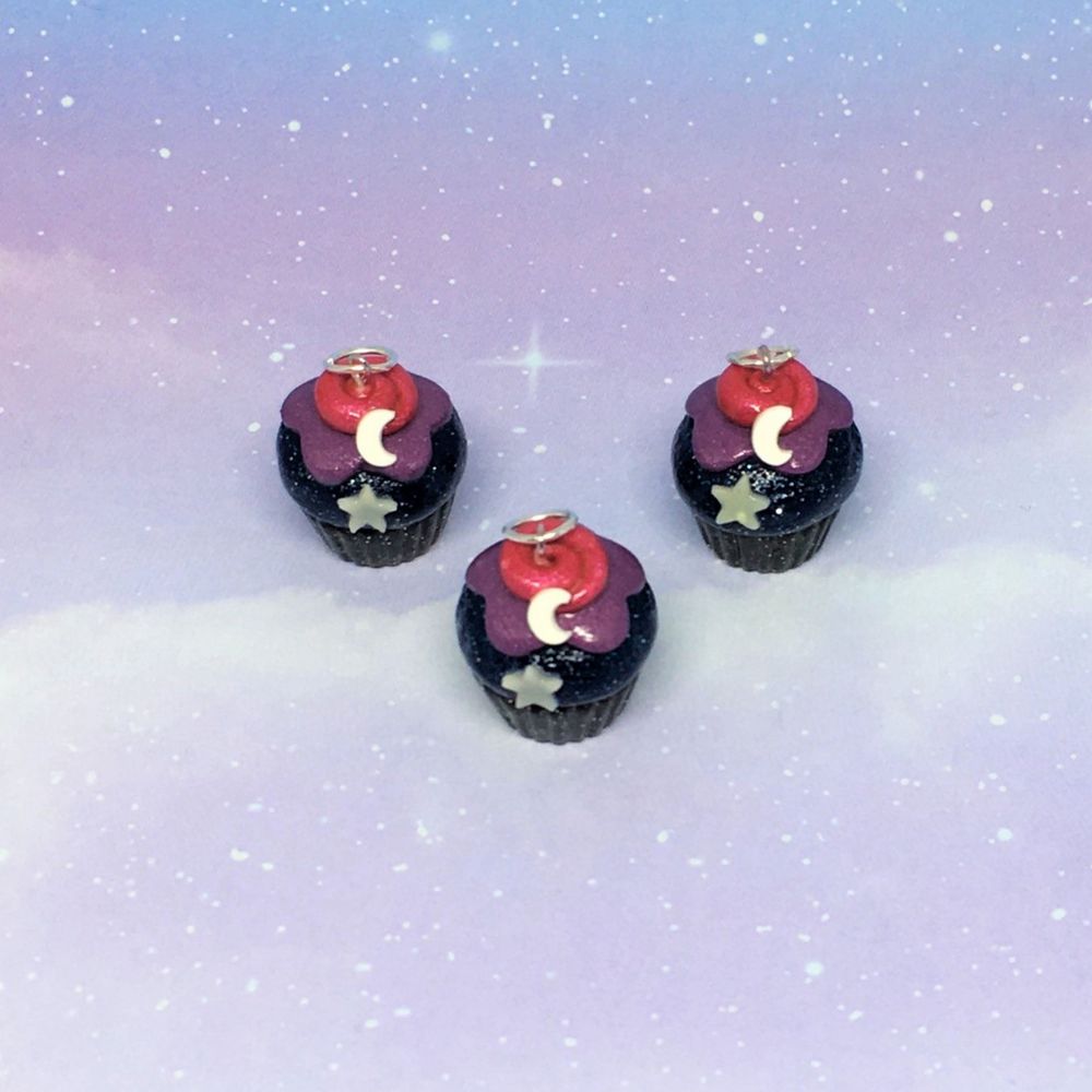 Three polymer clay cupcake charms.
The bottoms are sparkly black, the top is dark sparkly blue with sparkly purple frosting. A swirl of pink is on top with a crescent moon and glow in the dark star on each. They are facing the camera.