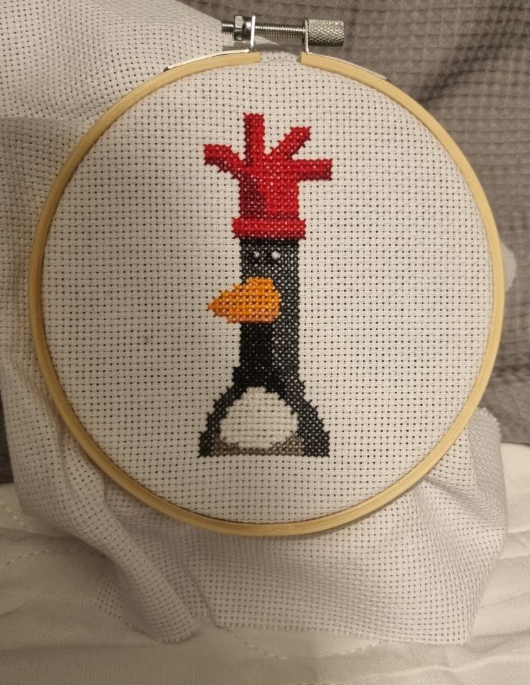 A cross stitch of convicted master felon and antagonist of Wallace and Gromit: Feathers McGraw. He is a plasticine penguin, wearing a red rubber glove as a cap to deceive people into thinking he is an innocent chicken when he is in fact a very evil and criminal penguin.