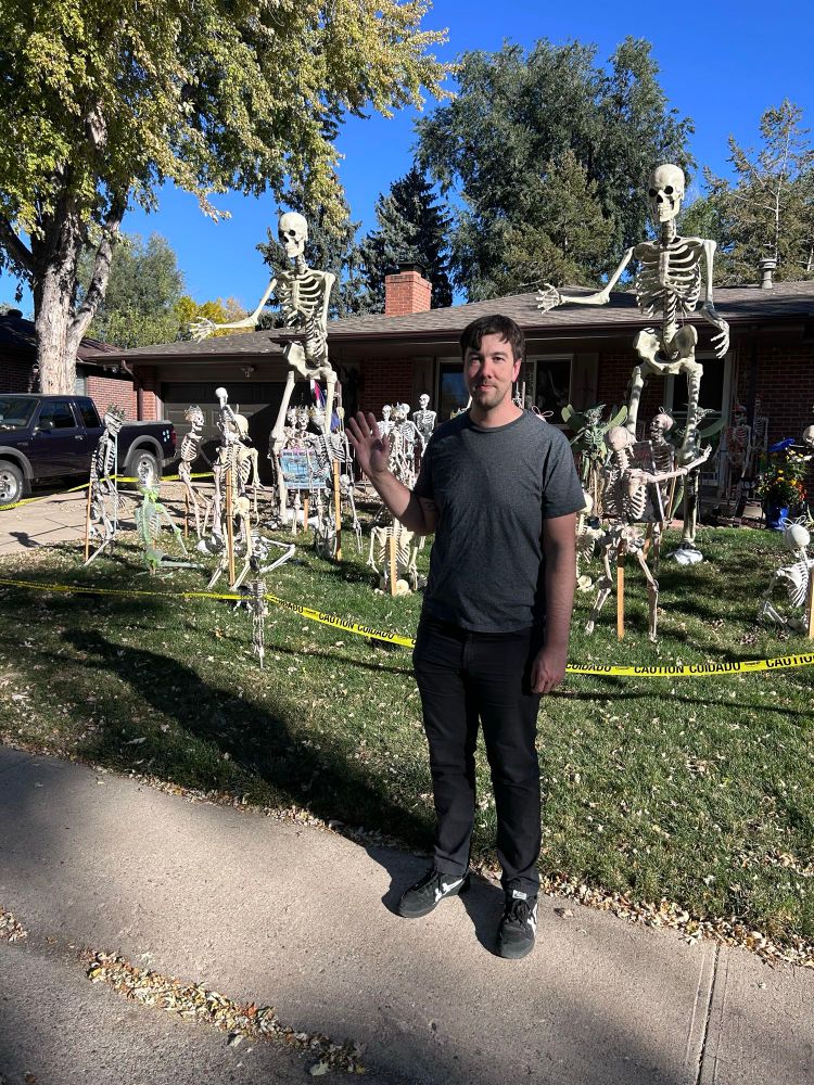 Corey from Broken Record waving in front of a lawn full of skeletons