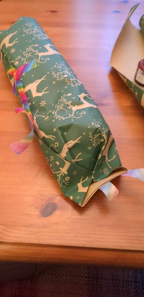 A half-wrapped present with rainbow washy tape peeling off from all over it