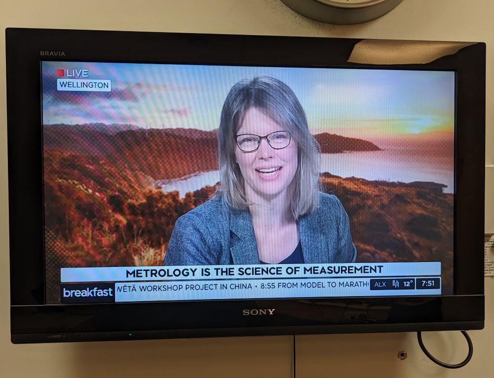 A photo of a tv. On screen is blonde woman in her late 40s wearing glasses. The text in front of her says 