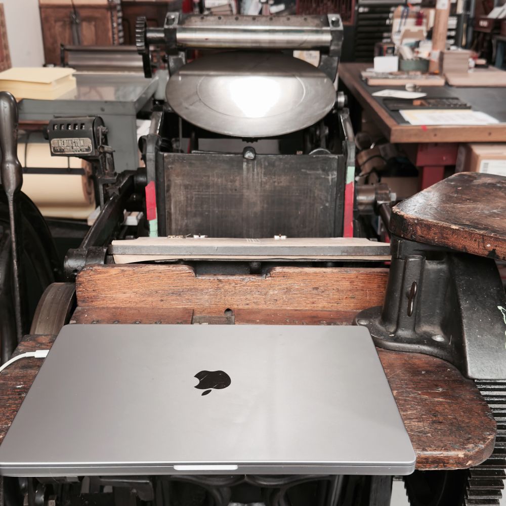 Printing press with laptop sitting on it. 