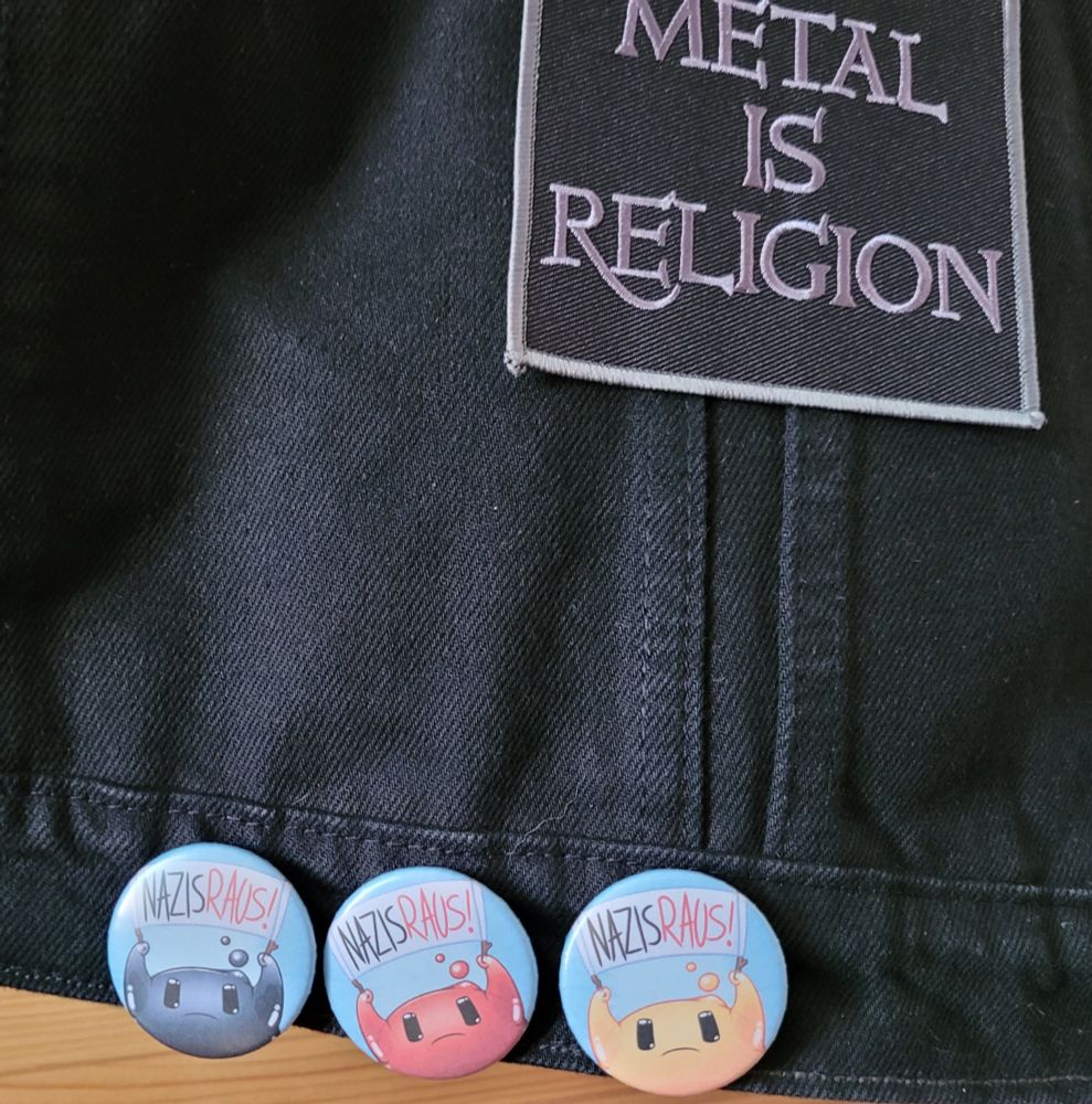 Am unteren Saum sind drei  Bittons mit Schildslimes in schwarz, rot und gelb, die "Nazis raus" sagen.