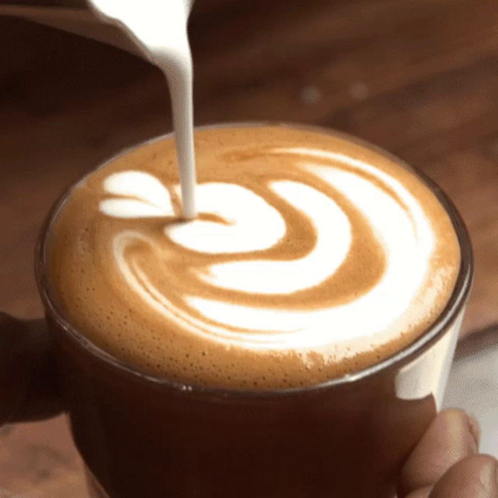 milk is being poured into a cup of cappuccino