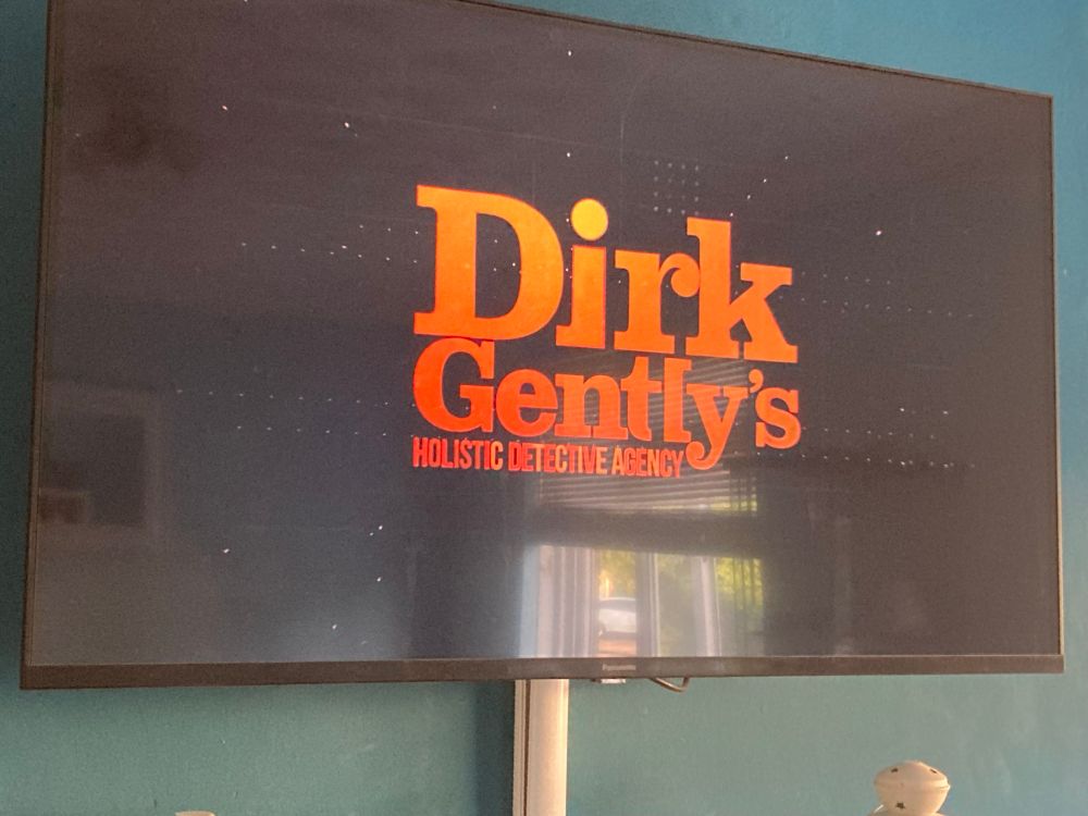 Photo of a TV screen open to the title of “Dirk Gently's Holistic Detective Agency” on Netflix.