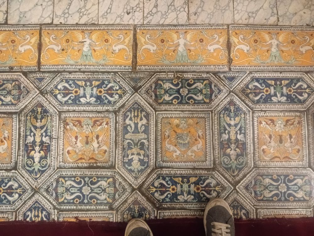 A tile floor features old school mermaids (the ones with a split tail) and other mythical beings.