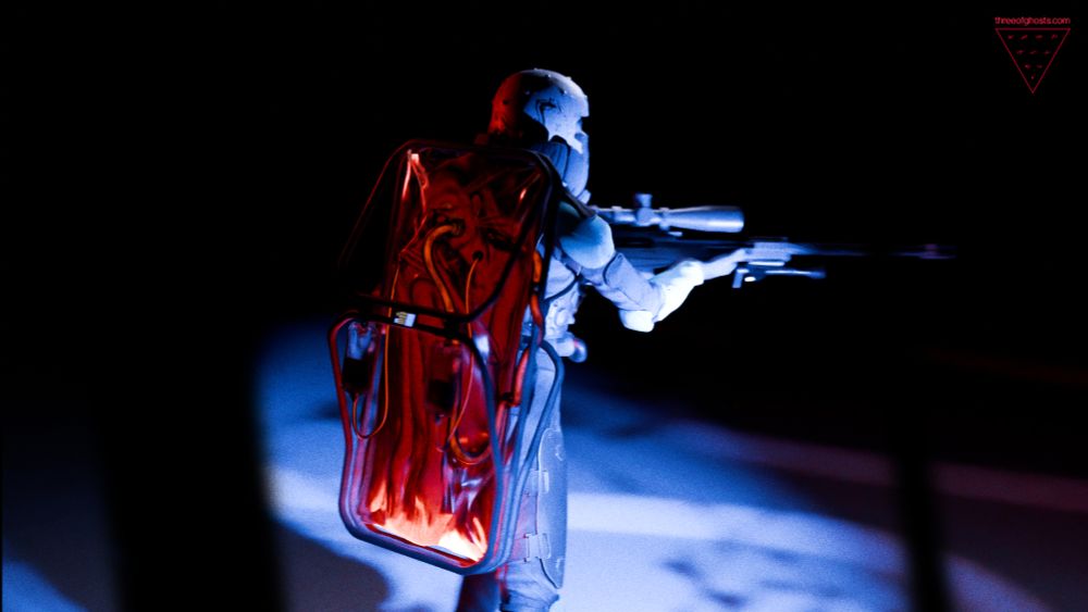 A shot of the soldier from behind, a corpse is sealed in a transparent body bag hanging from a frame attached to her back. Pipes and cables pump custom narcotics from it to the solider.