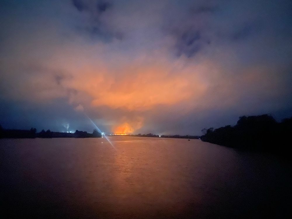 Photo from house boat on Clarence river NSW centre of the image is a burning sugar cane fire, casting a red glow on the surface of the river. The red orange colour is reflected onto the clouds with an attractive blue thrown at the horizon and the corners of the image. Looking at the Harwood bridge and sugar cane mill.